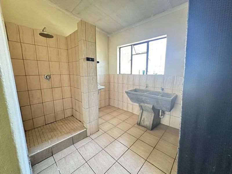 A functional bathroom featuring a tiled shower enclosure, concrete double sink, and tiled flooring, offering potential for modernization and cosmetic updates.