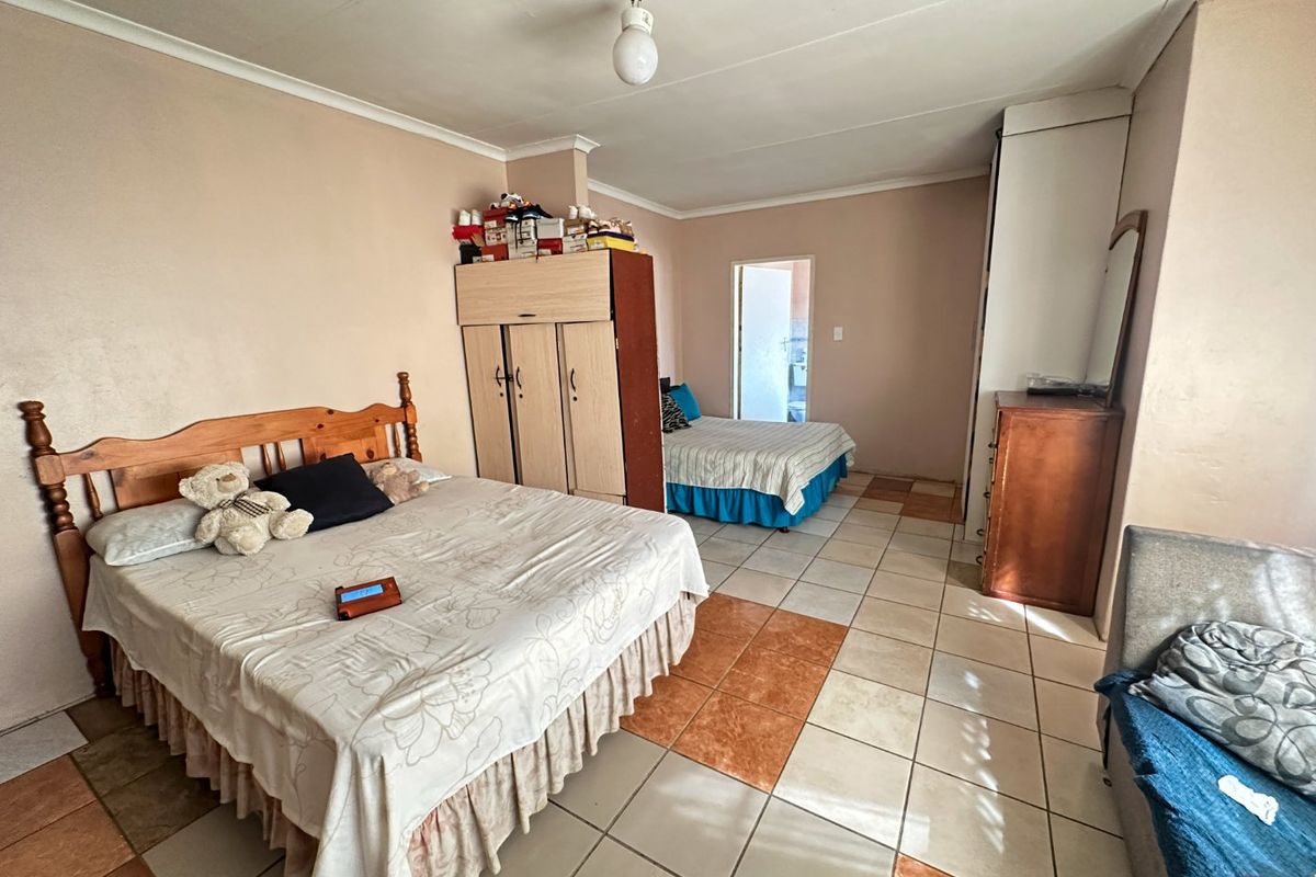 Spacious bedroom featuring tiled flooring and built-in wardrobe storage, offering a functional layout with direct access to an adjoining room.