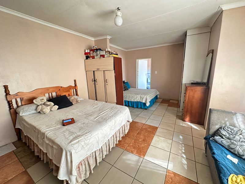 Spacious bedroom featuring tiled flooring and built-in wardrobe storage, offering a functional layout with direct access to an adjoining room.