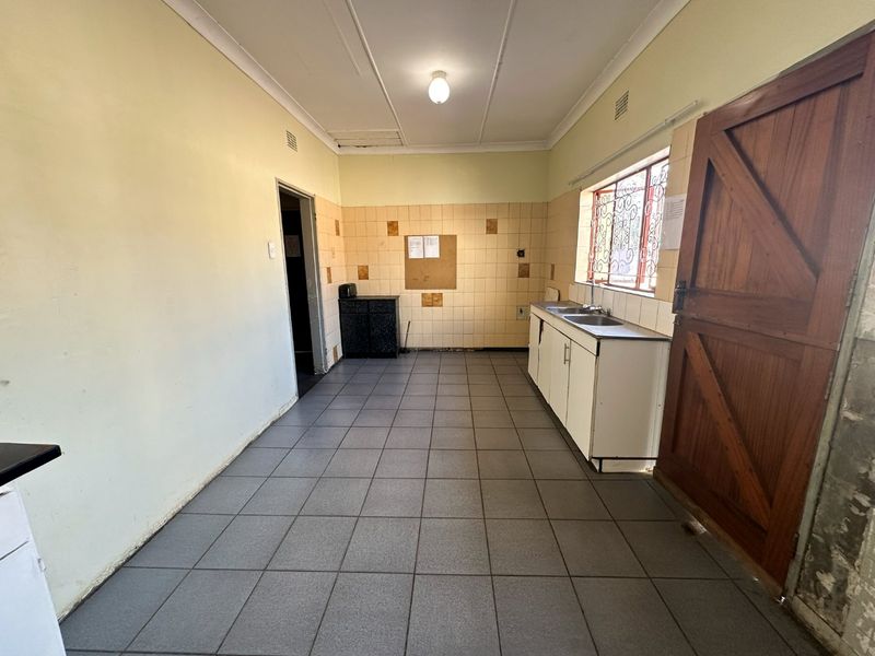 A functional, empty kitchen space featuring tiled flooring, a built-in sink unit, and tiled splashbacks, offering a blank canvas for renovation.