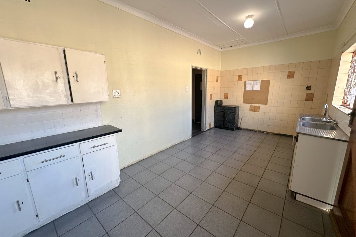 A functional, empty kitchen featuring tiled flooring, built-in cabinetry, and a double bowl sink, offering a blank canvas for renovation and modernization.