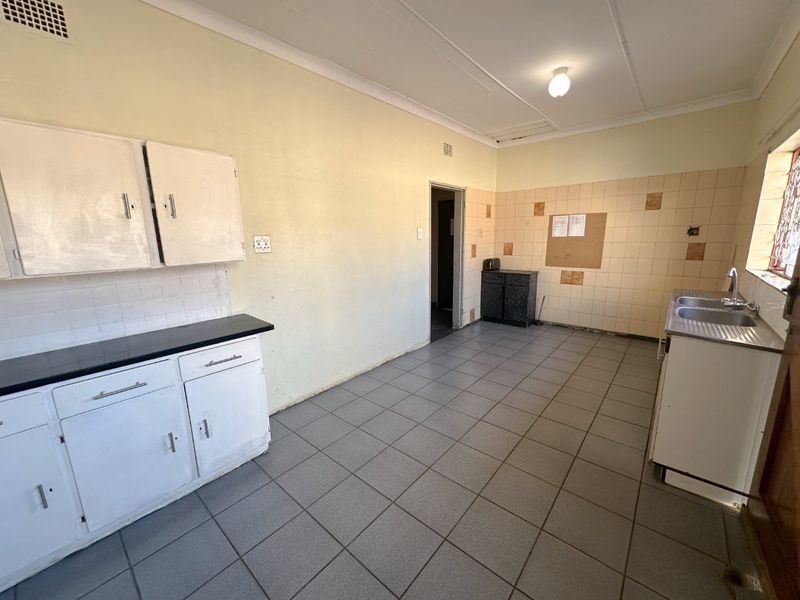 A functional, empty kitchen featuring tiled flooring, built-in cabinetry, and a double bowl sink, offering a blank canvas for renovation and modernization.