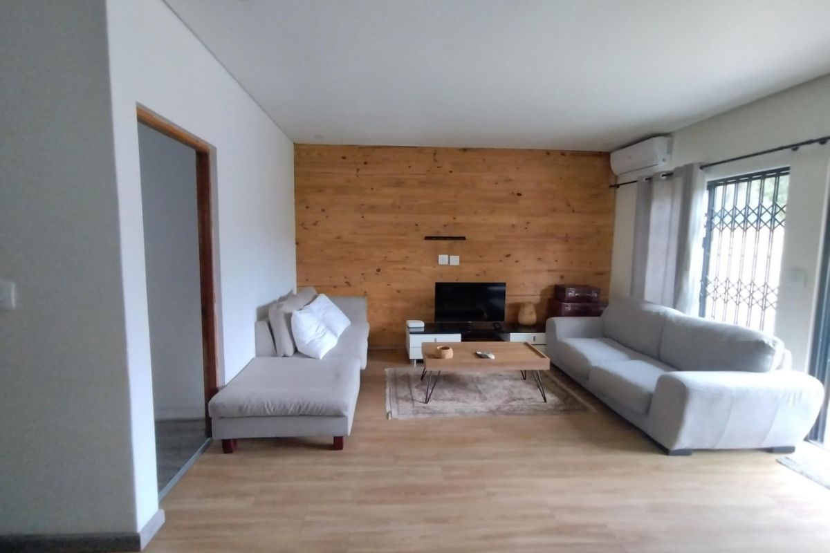 A well-maintained living room featuring a warm wood-paneled accent wall, light laminate flooring, and a split-system air conditioner for climate control.