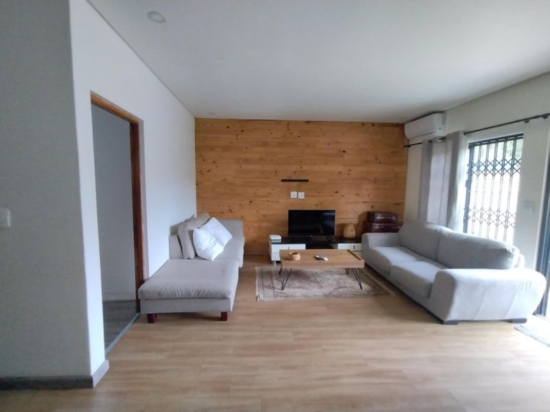 A well-maintained living room featuring a warm wood-paneled accent wall, light laminate flooring, and a split-system air conditioner for climate control.