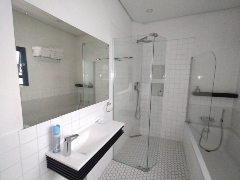 Modern bathroom featuring a wall-mounted vanity, large mirror, glass-enclosed shower with a rain head, and a separate bathtub with white tiled finishes.