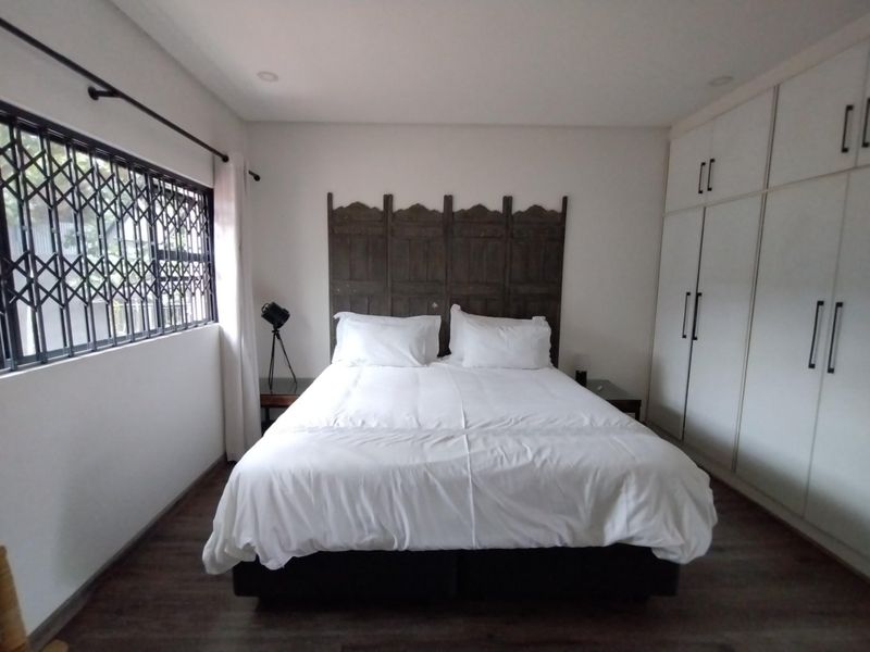 A well-maintained bedroom featuring built-in cupboards, laminate flooring, recessed lighting, and a security gate on the window.