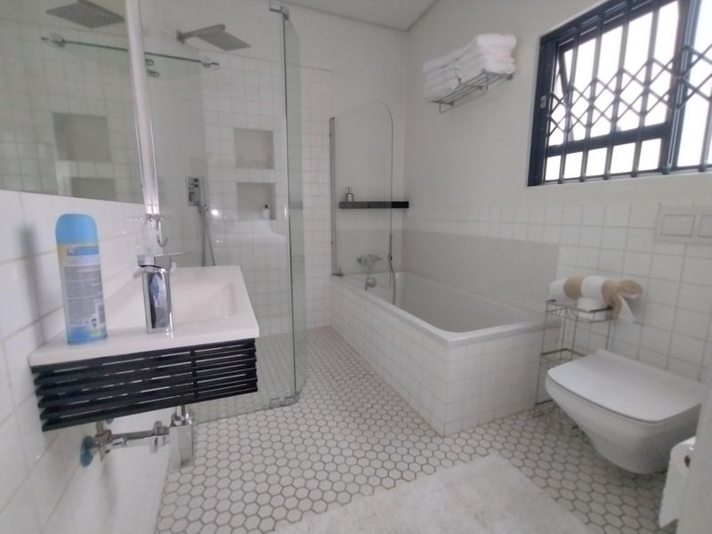 Modern bathroom featuring a wall-mounted vanity, glass-enclosed shower, built-in bathtub, and wall-hung toilet with contemporary hexagonal floor tiling.