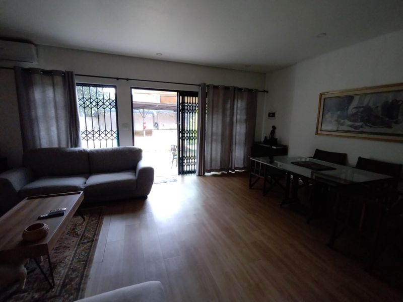 Open-plan living and dining area featuring laminate flooring, recessed lighting, and direct access to the exterior through a sliding glass door with security gate.