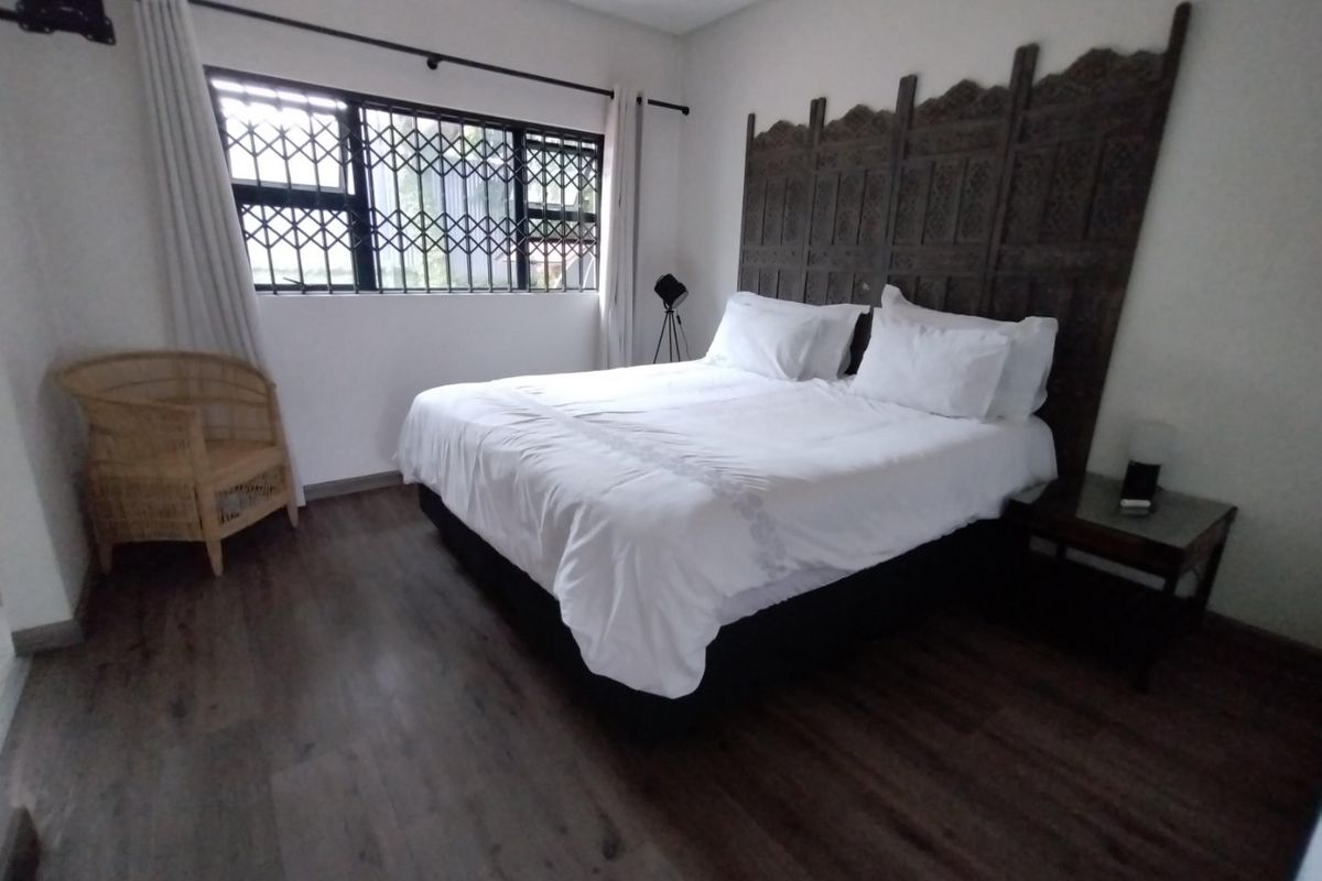 A well-maintained bedroom featuring dark laminate flooring, recessed ceiling lights, and a window fitted with a security gate.
