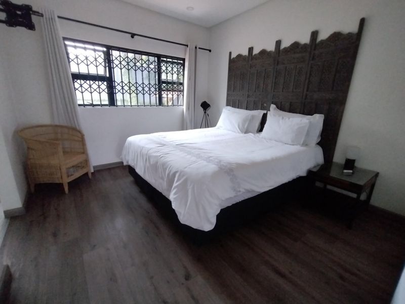 A well-maintained bedroom featuring dark laminate flooring, recessed ceiling lights, and a window fitted with a security gate.