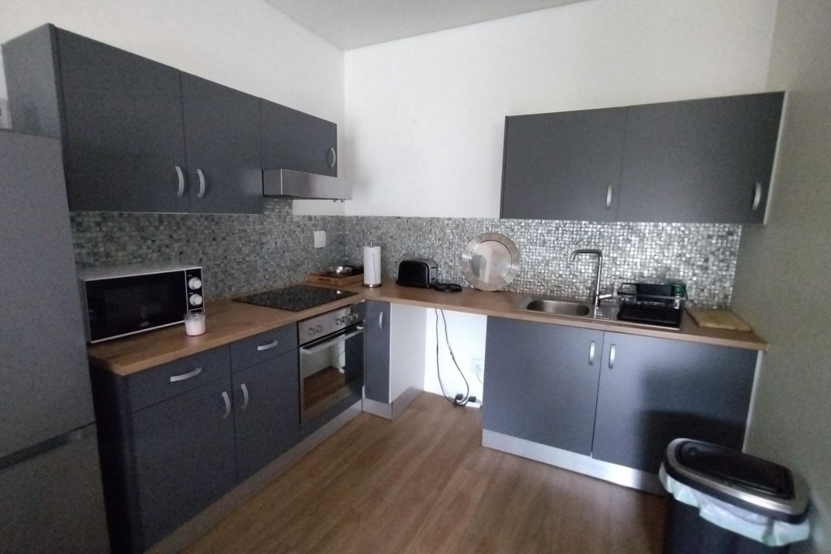 Modern kitchen featuring dark grey cabinetry, wood-look countertops, mosaic tile backsplash, and integrated stainless steel appliances.