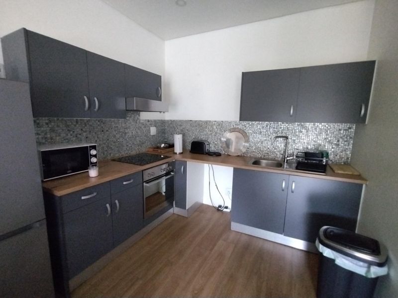 Modern kitchen featuring dark grey cabinetry, wood-look countertops, mosaic tile backsplash, and integrated stainless steel appliances.