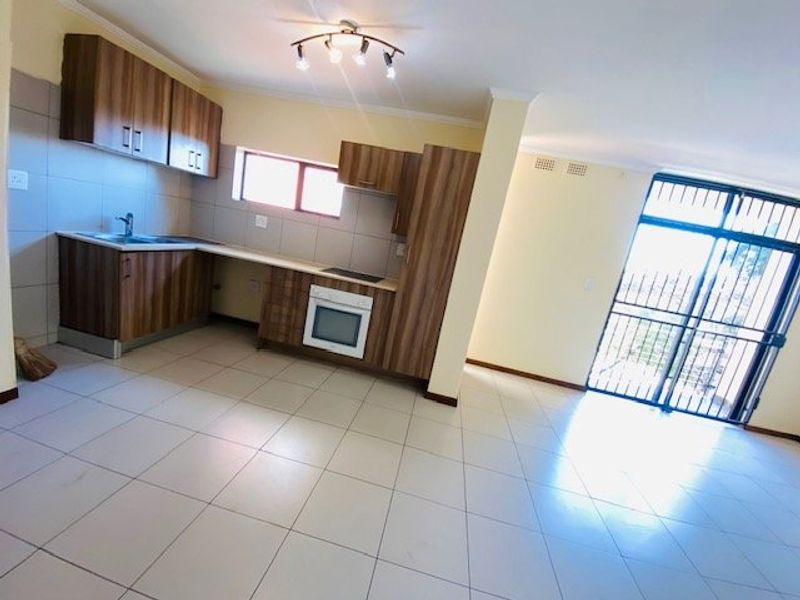 Open-plan kitchen and living area featuring tiled flooring, built-in cabinetry with integrated oven and hob, and access to a secure exterior entrance.