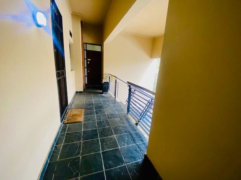 A covered apartment balcony featuring slate tile flooring, a metal safety balustrade, and a secure entrance gate.