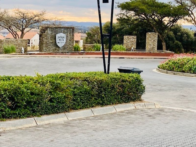 Entrance view of the Jackal Creek estate featuring stone-clad signage, paved driveway, and manicured landscaping.