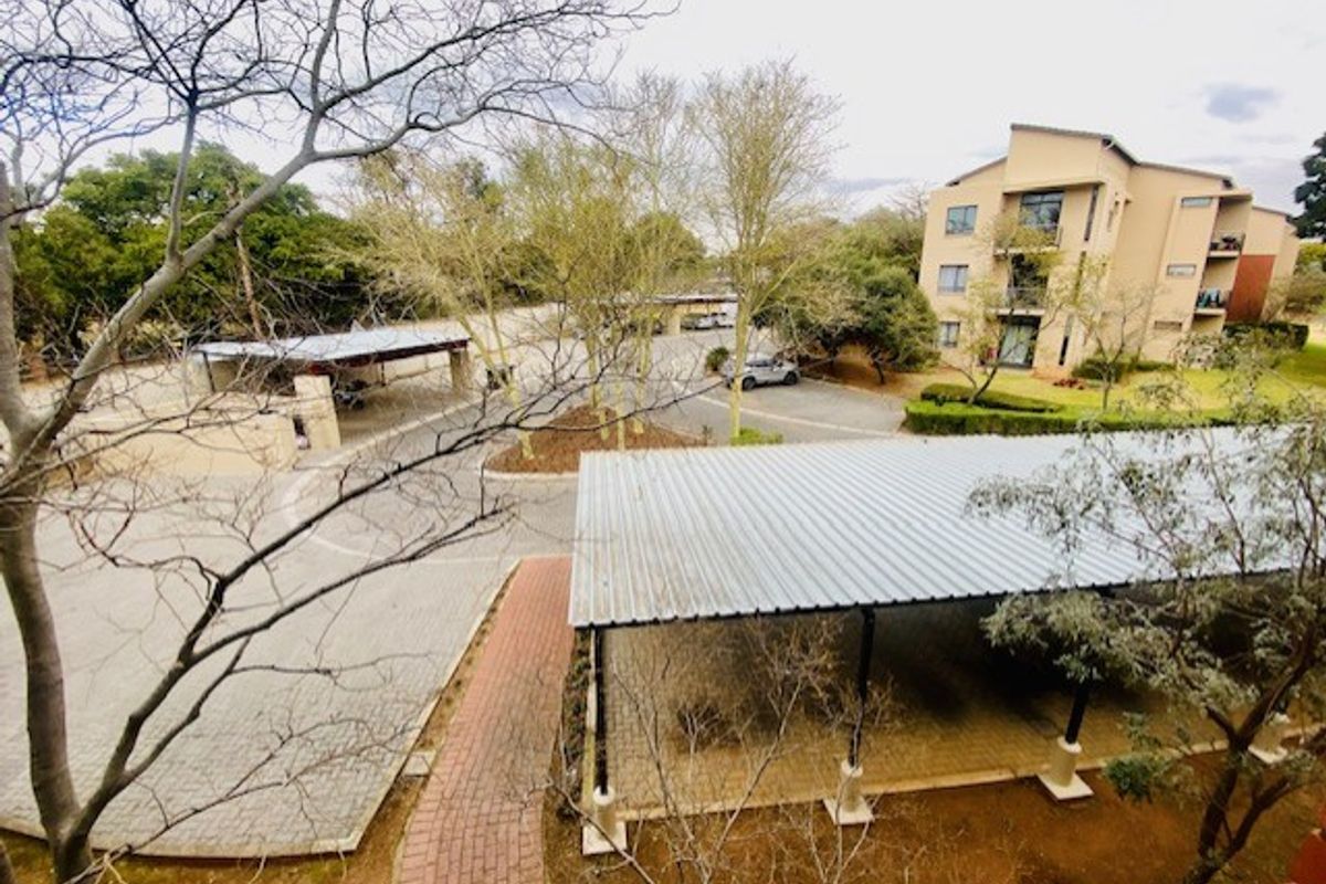 An elevated view of the apartment complex grounds, featuring covered parking bays, paved driveways, and established garden areas.