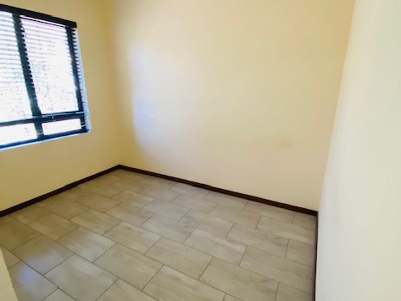 A bright, empty bedroom featuring neutral tiled flooring and fitted venetian blinds, offering a clean and versatile space ready for personalization.