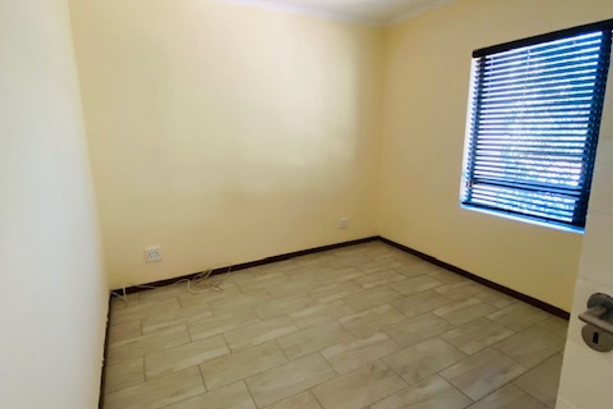 A clean, empty bedroom featuring neutral yellow walls, modern wood-look tiled flooring, and window blinds, ready for personalization.