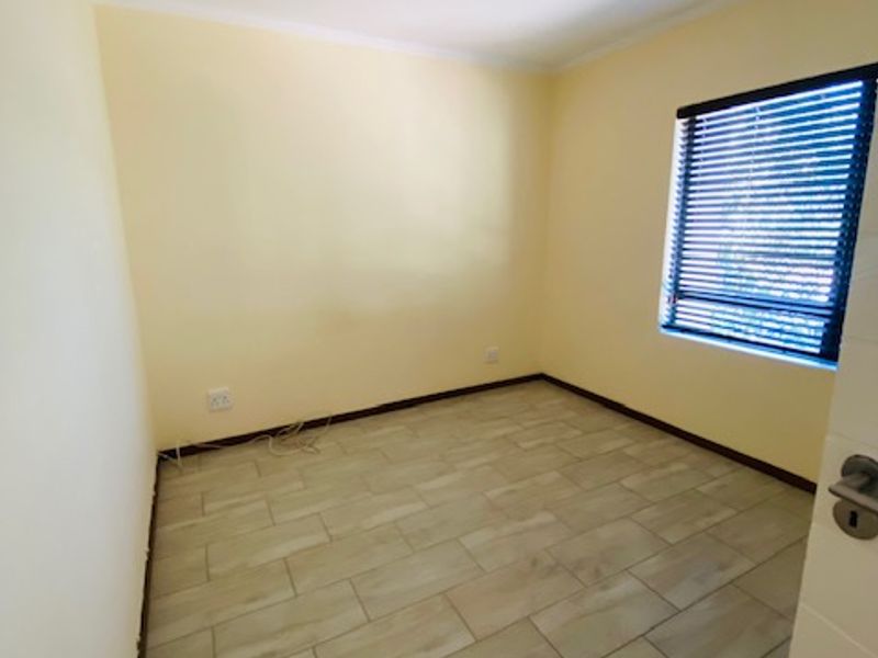 A clean, empty bedroom featuring neutral yellow walls, modern wood-look tiled flooring, and window blinds, ready for personalization.