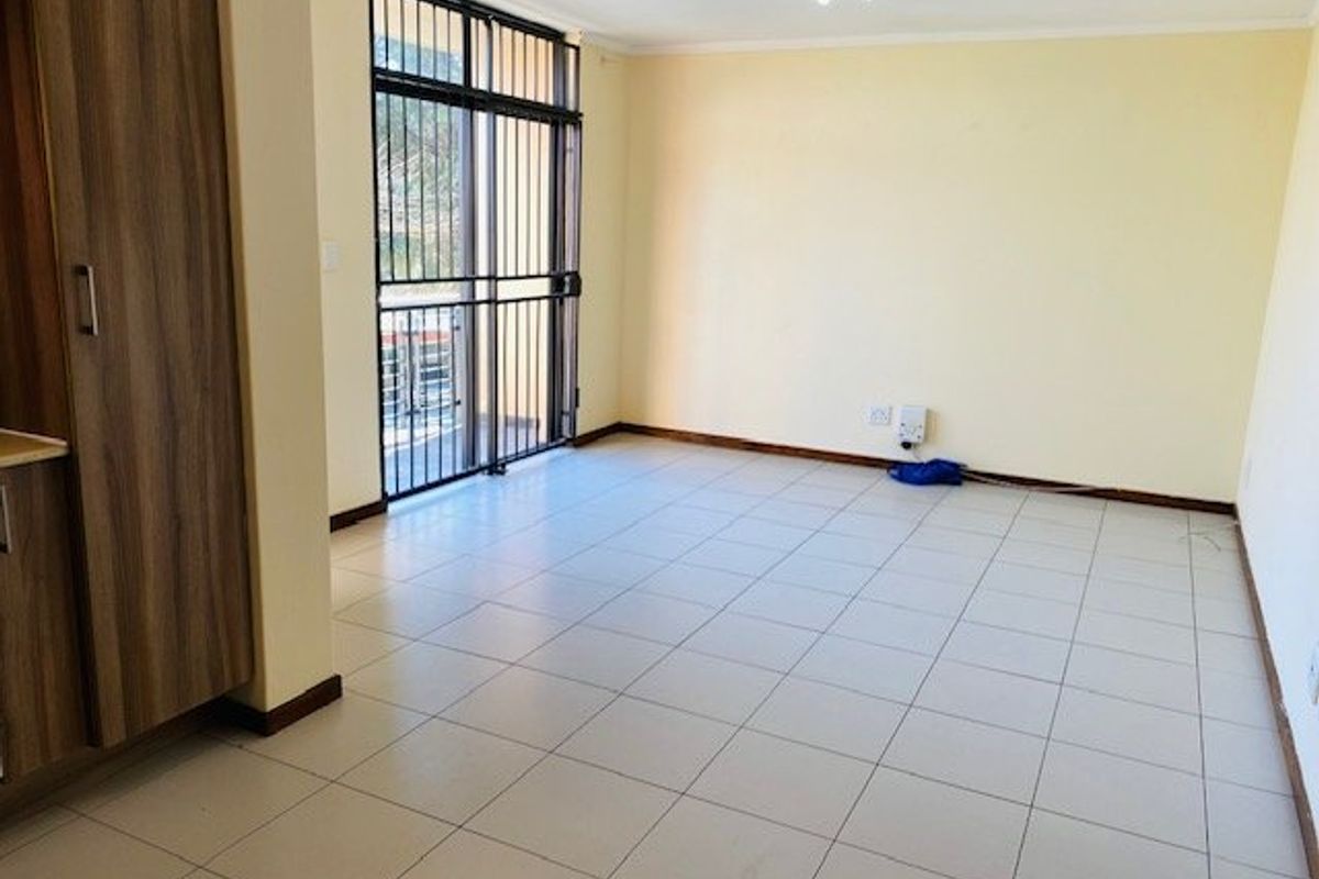 An empty, tiled living area featuring built-in cabinetry and a sliding door with a security gate leading to an outdoor space.