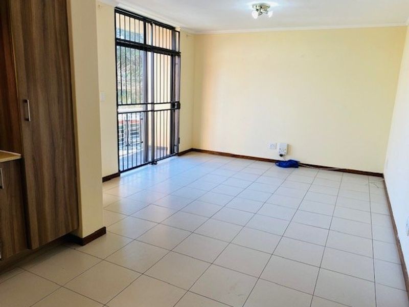 An empty, tiled living area featuring built-in cabinetry and a sliding door with a security gate leading to an outdoor space.