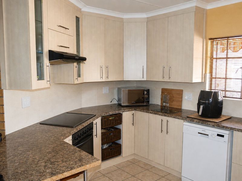 Functional kitchen featuring light wood-finish cabinetry, dark laminate countertops, built-in oven with hob, extractor fan, and tiled flooring.