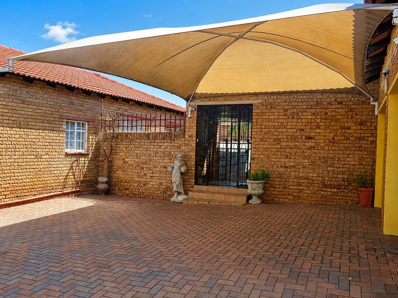 A paved outdoor patio area featuring a large shade sail, face brick construction, and a secure entrance gate.