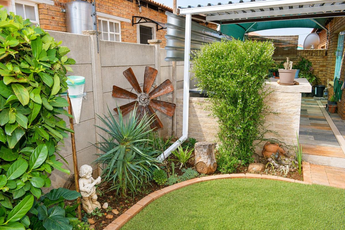 A well-maintained rear garden area featuring a precast concrete boundary wall, a built-in stone-clad counter, and a covered patio section.