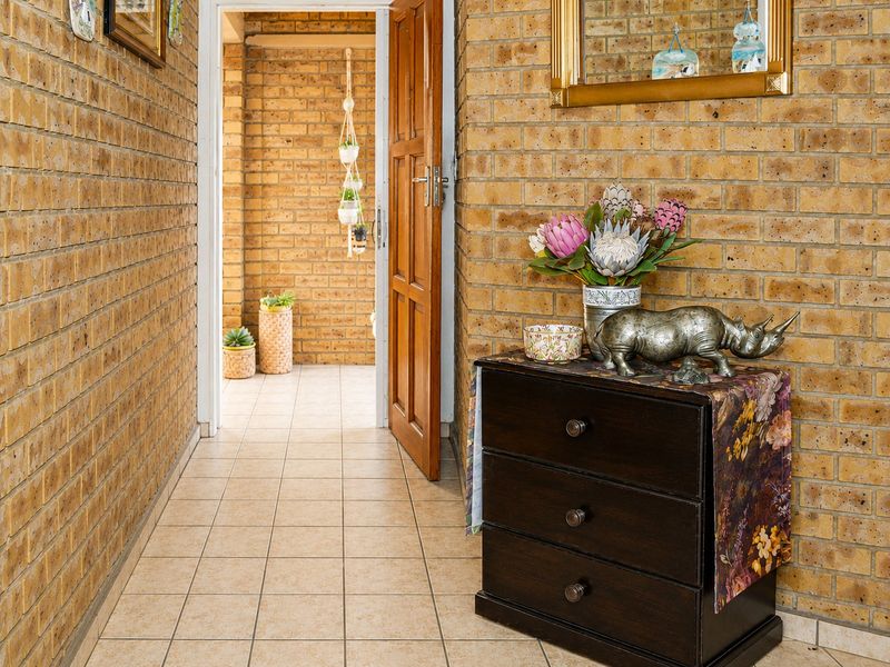 A hallway featuring exposed brick walls and ceramic floor tiles, leading through a timber door to an adjacent outdoor area.