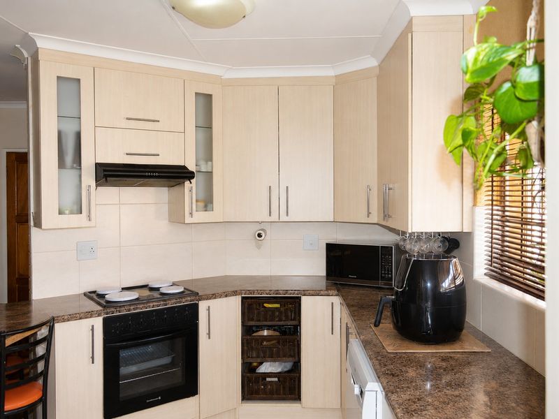 A functional kitchen featuring light wood-tone cabinetry, granite-look laminate countertops, a built-in oven with electric hob, and a tiled backsplash.