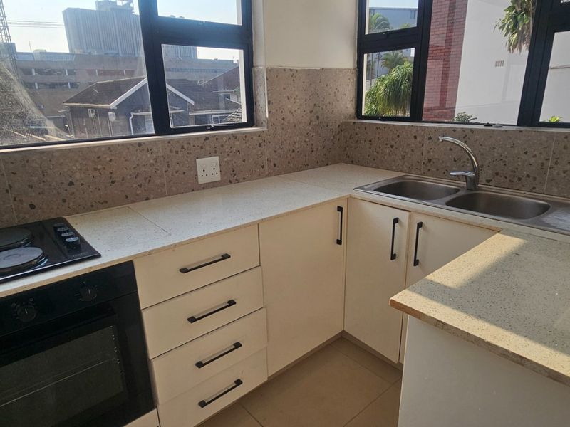 A clean, modern kitchen featuring built-in cabinetry, quartz countertops, an integrated electric hob and oven, and a double bowl sink with large windows.