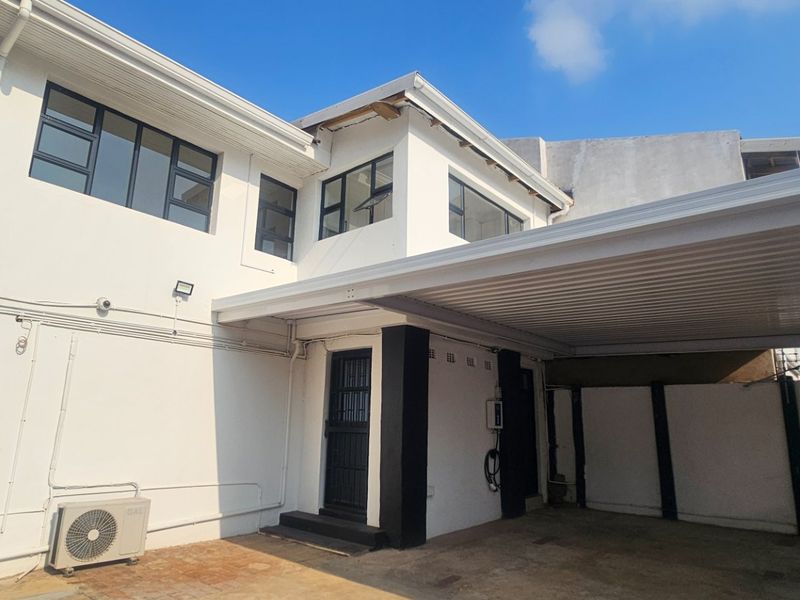 Exterior view of the apartment building featuring a covered carport, security gate, and external air conditioning unit.