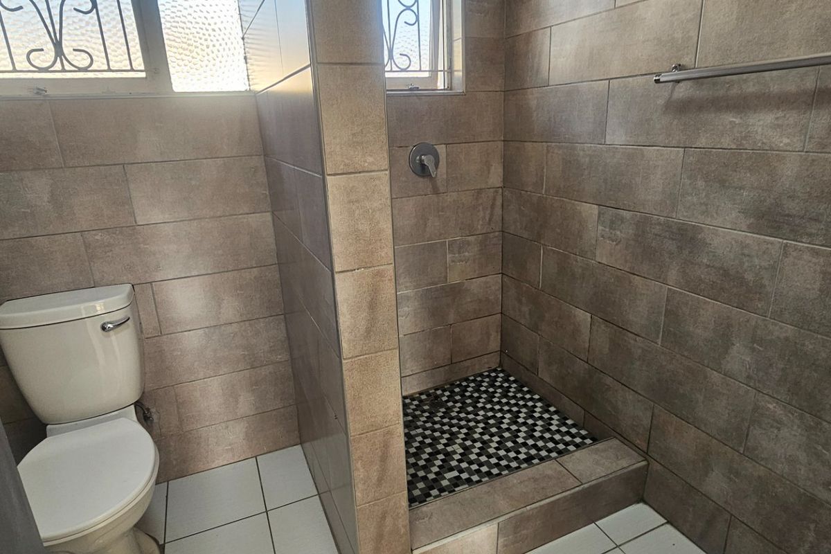 A clean, functional bathroom featuring a walk-in shower with mosaic floor tiling, a standard toilet, and neutral wall tiles.