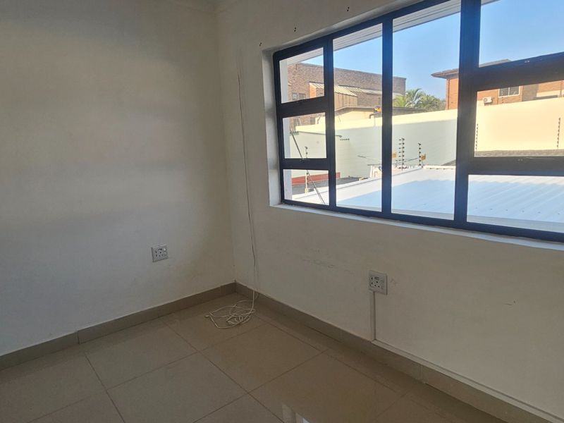 An empty bedroom featuring tiled flooring, neutral walls, and large aluminium-framed windows providing natural light.