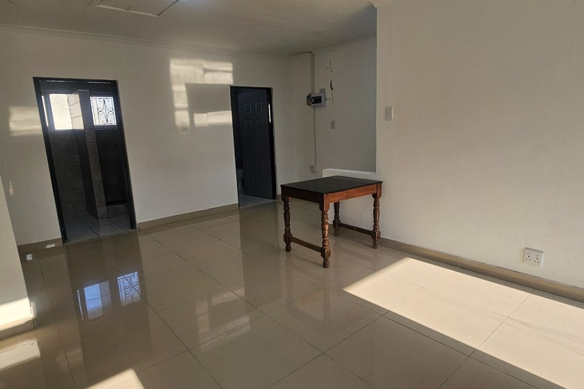 An empty, open-plan living area featuring neutral tiled flooring and access to adjacent rooms, providing a blank canvas for interior design.