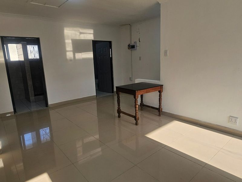 An empty, open-plan living area featuring neutral tiled flooring and access to adjacent rooms, providing a blank canvas for interior design.