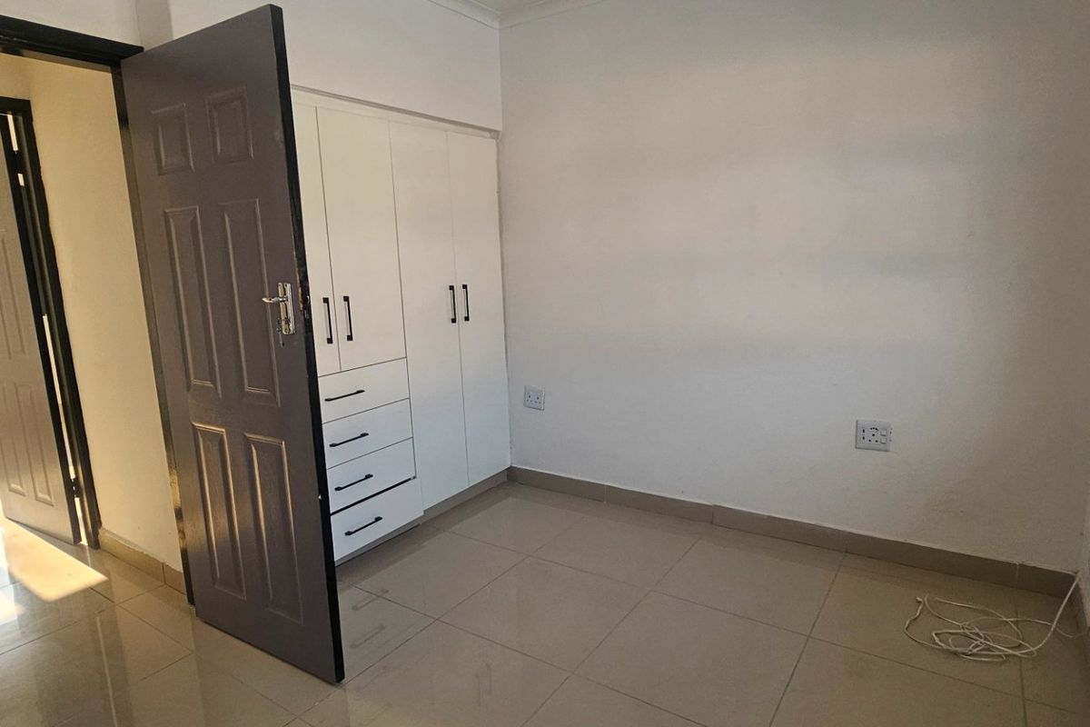 A clean, empty bedroom featuring neutral tiled flooring, built-in cupboards, and natural light from the side window.