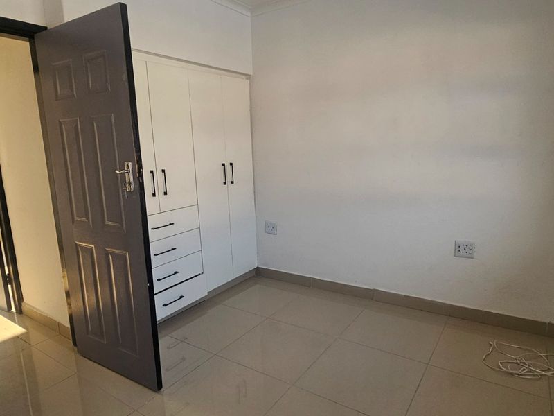 A clean, empty bedroom featuring neutral tiled flooring, built-in cupboards, and natural light from the side window.