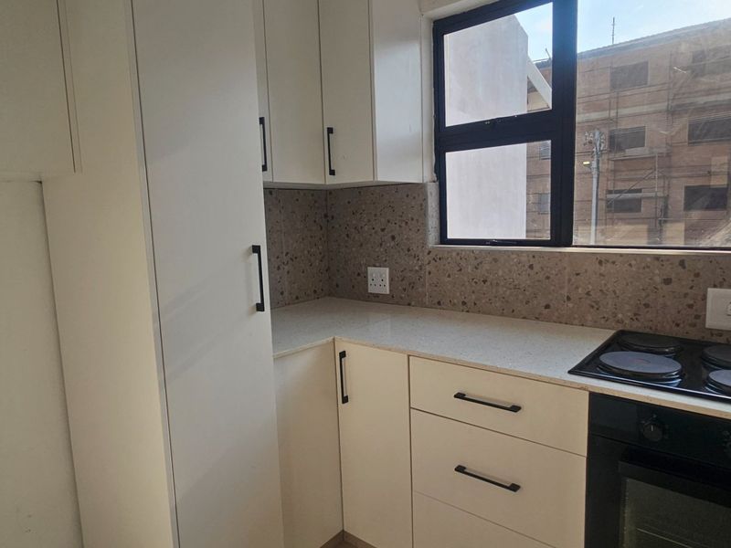 Modern kitchen featuring white built-in cabinetry, stone countertops, a terrazzo-style backsplash, and integrated electric hob and oven.