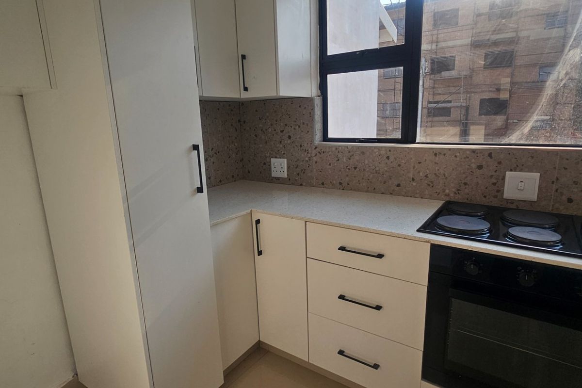 Modern kitchen featuring white built-in cabinetry, stone countertops, a terrazzo-style backsplash, and integrated electric hob and oven.