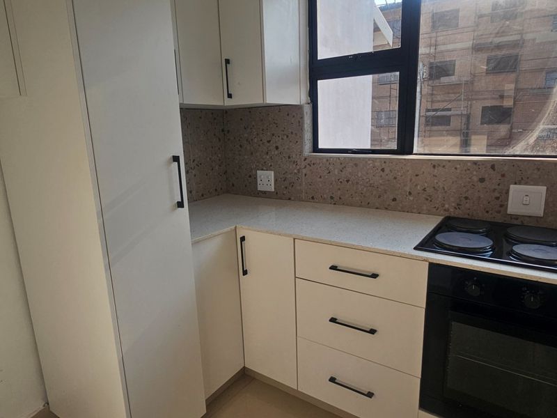 Modern kitchen featuring white built-in cabinetry, stone countertops, a terrazzo-style backsplash, and integrated electric hob and oven.