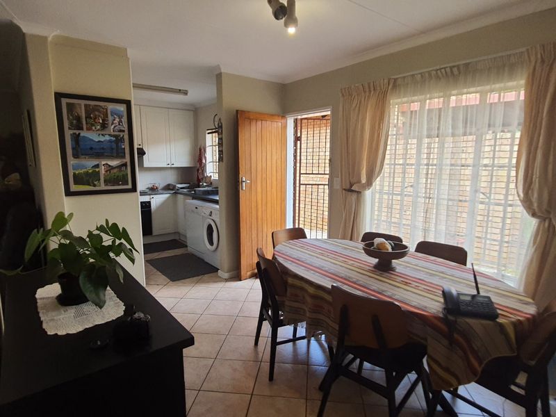 Open plan dining area adjacent to a functional kitchen with tiled flooring and direct access to an outdoor space via a security gate.