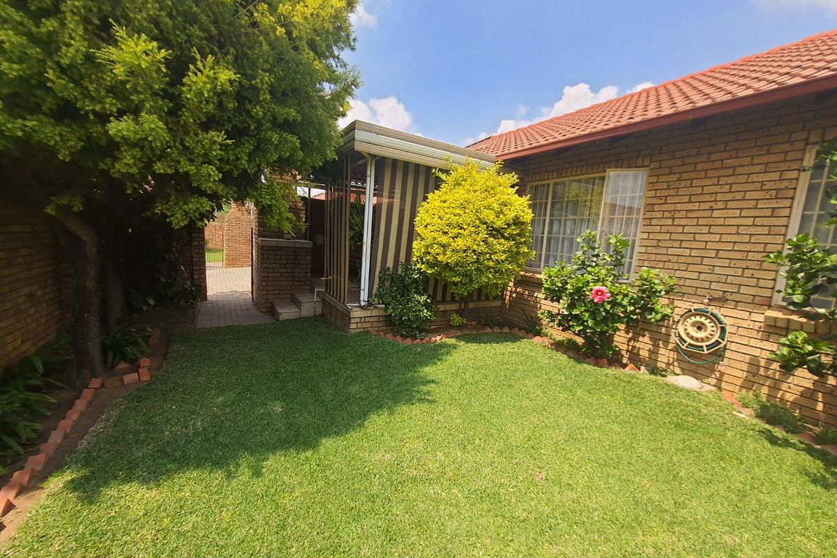 A well-maintained rear garden featuring a brick townhouse facade, a small lawn, and a covered patio area.