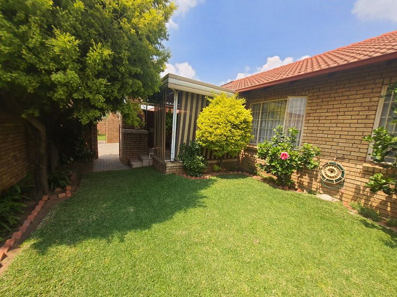 A well-maintained rear garden featuring a brick townhouse facade, a small lawn, and a covered patio area.