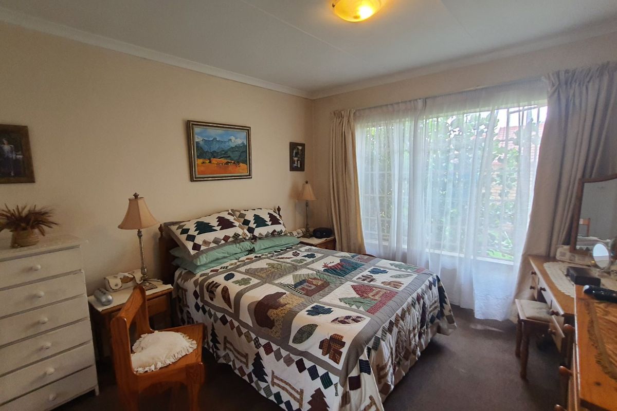 A cozy bedroom featuring neutral walls, carpeted flooring, and a large window with curtains, providing natural light and a view of the exterior.