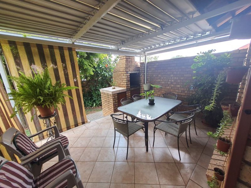 Covered outdoor patio featuring a built-in brick braai, tiled flooring, and a corrugated metal roof, providing a functional space for outdoor dining and entertainment.