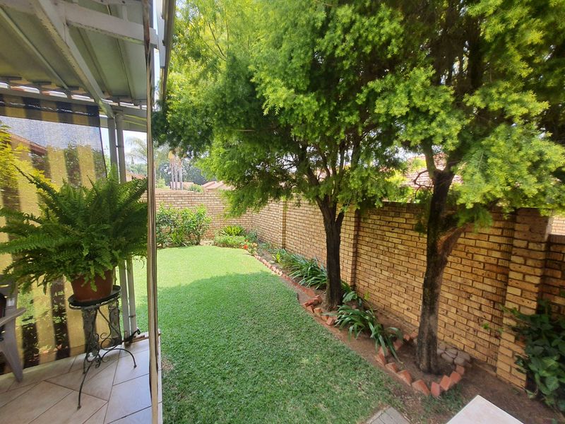 A private rear garden featuring a well-maintained lawn, mature trees, and a brick boundary wall, adjacent to a covered patio area.