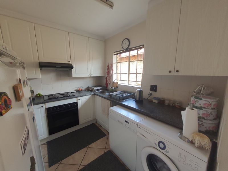 A functional kitchen featuring white cabinetry, dark laminate countertops, an electric hob with extractor, and tiled flooring with space for under-counter appliances.