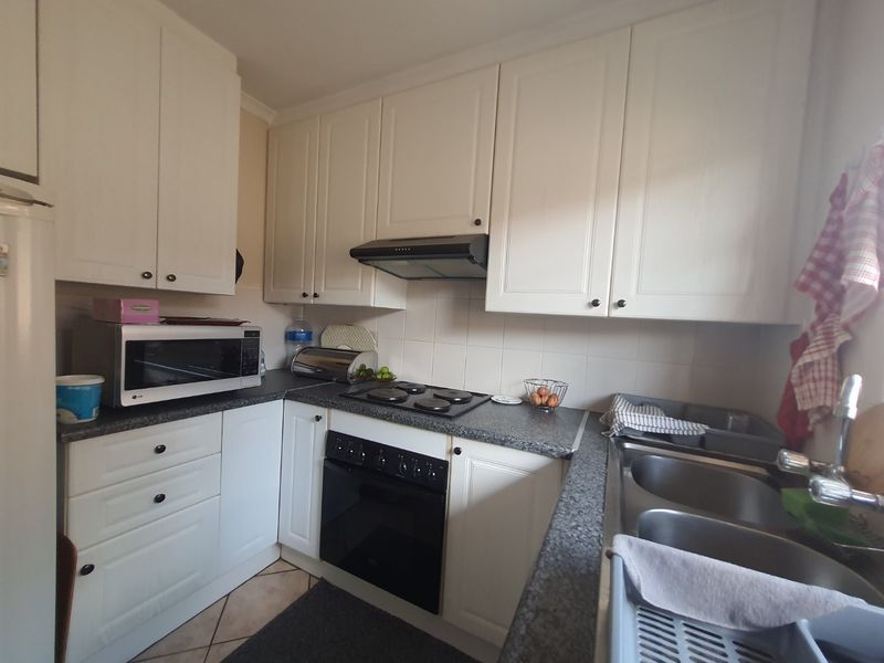 Compact kitchen featuring white cabinetry, dark laminate countertops, built-in oven, electric hob, extractor fan, and a double bowl sink with tiled backsplash.