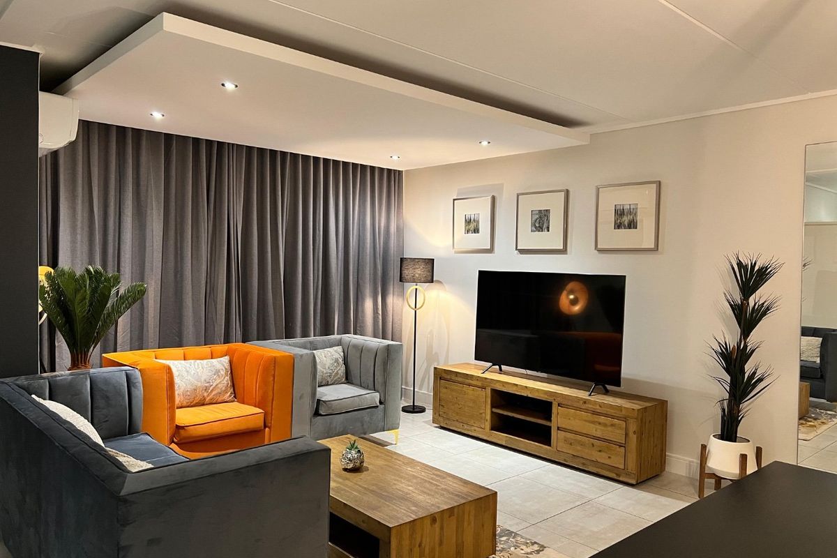 A well-maintained living room featuring tiled flooring, a modern recessed ceiling with integrated downlights, and a wall-mounted air conditioning unit.